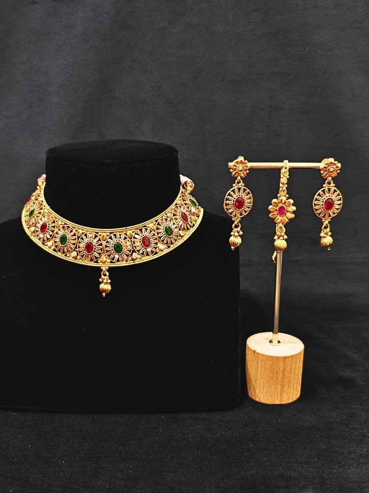 Close-up of an ornate traditional Red & Green Diamond gold Polish Choker jewellery set and earrings and maangtikka with Baguette American Diamonds and Red and Green Colored Stones. A luxury American diamond necklace set styled beautifully for a wedding guest look in India. Close-up of a featuring an anti-tarnish American diamond artificial necklace.