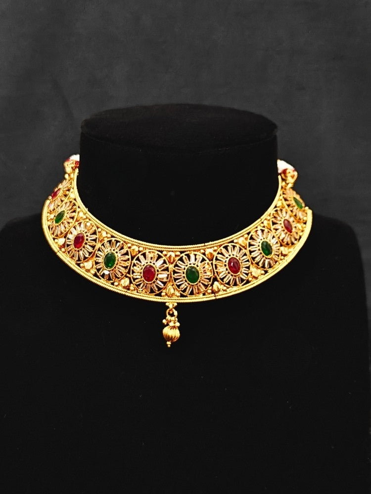 Close-up of an ornate traditional Red & Green Diamond gold Polish Choker jewellery set and earrings and maangtikka with Baguette American Diamonds and Red and Green Colored Stones. A luxury American diamond necklace set styled beautifully for a wedding guest look in India. Close-up of a featuring an anti-tarnish American diamond artificial necklace.