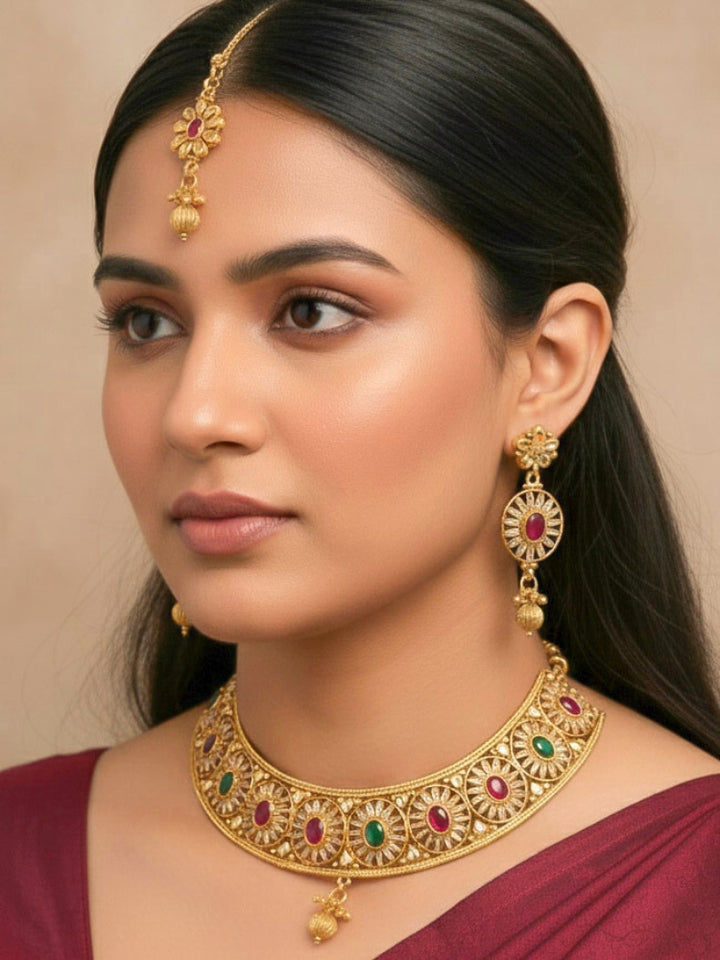 Close-up of a woman wearing an ornate traditional Red & Green Diamond gold Polish Choker jewellery set and earrings and maangtikka with Baguette American Diamonds and Red and Green Colored Stones. A woman wearing a luxury American diamond necklace set styled beautifully for a wedding guest look in India. Close-up of a featuring an anti-tarnish American diamond artificial necklace.
