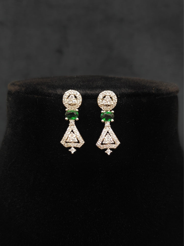 Close-up of an ornate Western Green (Silver Polish) Collar Diamond jewellery set and earrings with American Diamond and Green Colored Stones. Reception-ready look featuring a statement American diamond jewelry set. Party wear outfit completed with a lightweight American diamond necklace.