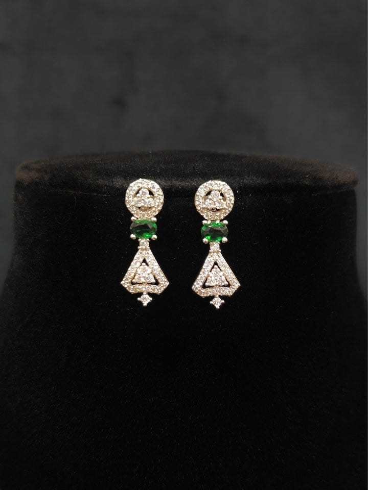 Close-up of an ornate Western Green (Silver Polish) Collar Diamond jewellery set and earrings with American Diamond and Green Colored Stones. Reception-ready look featuring a statement American diamond jewelry set. Party wear outfit completed with a lightweight American diamond necklace.