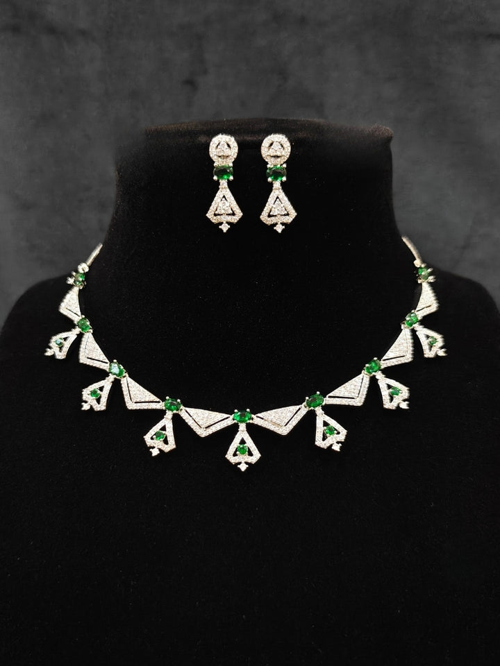 Close-up of an ornate Western Green (Silver Polish) Collar Diamond jewellery set and earrings with American Diamond and Green Colored Stones. Reception-ready look featuring a statement American diamond jewelry set. Party wear outfit completed with a lightweight American diamond necklace.