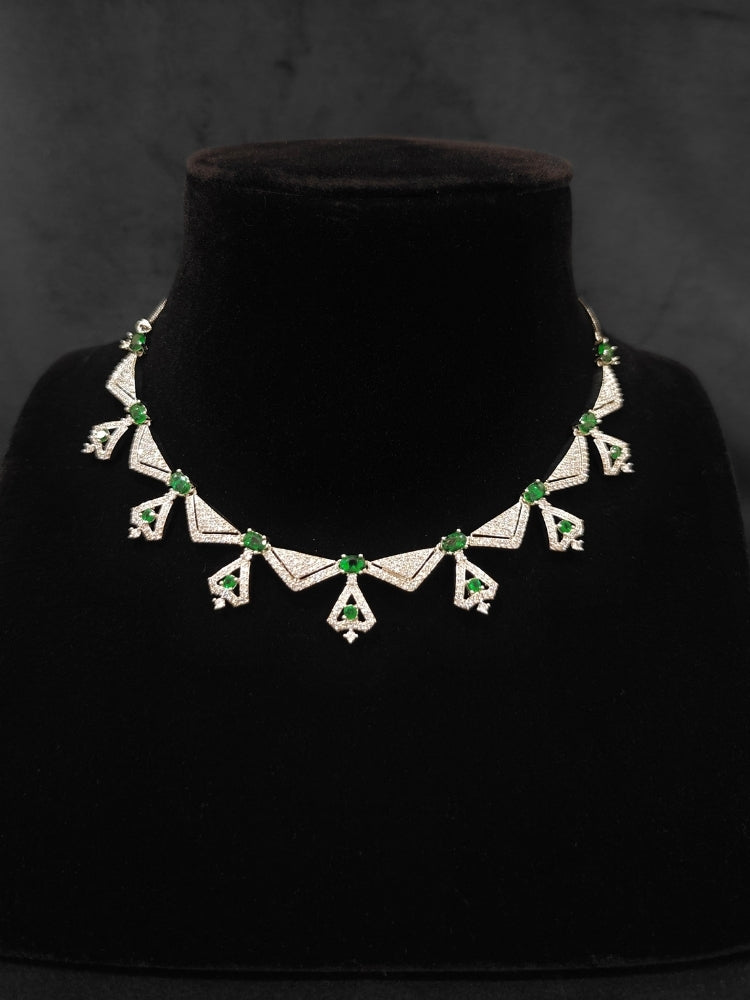 Close-up of an ornate Western Green (Silver Polish) Collar Diamond jewellery set and earrings with American Diamond and Green Colored Stones. Reception-ready look featuring a statement American diamond jewelry set. Party wear outfit completed with a lightweight American diamond necklace.