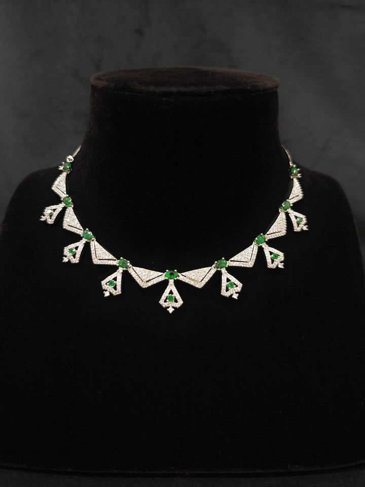 Close-up of an ornate Western Green (Silver Polish) Collar Diamond jewellery set and earrings with American Diamond and Green Colored Stones. Reception-ready look featuring a statement American diamond jewelry set. Party wear outfit completed with a lightweight American diamond necklace.
