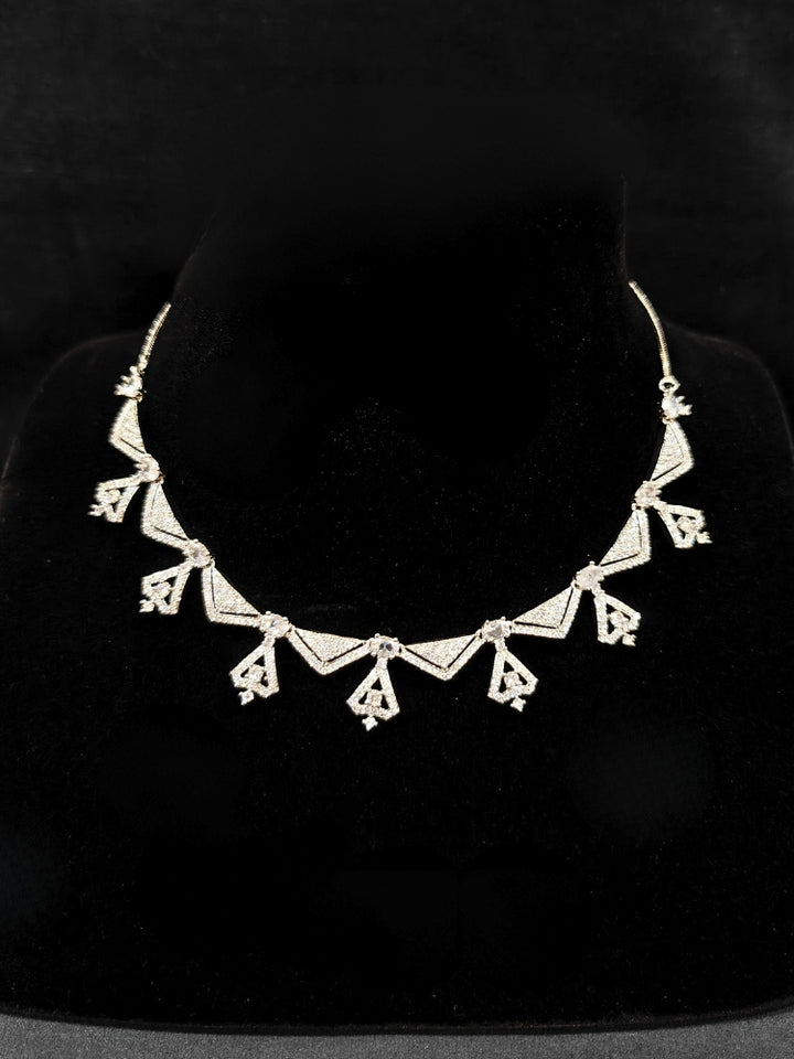 Close-up of an ornate Western White (Silver Polish) Collar Diamond jewellery set and earrings with American Diamond. Reception-ready look featuring a statement American diamond jewelry set. Party wear outfit completed with a lightweight American diamond necklace.