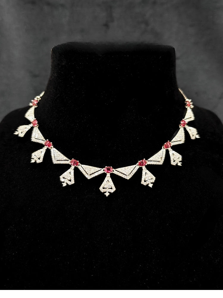 Close-up of an ornate Western Red (Silver Polish) Collar Diamond jewellery set and earrings with American Diamond and Green Colored Stones. Reception-ready look featuring a statement American diamond jewelry set. Party wear outfit completed with a lightweight American diamond necklace.