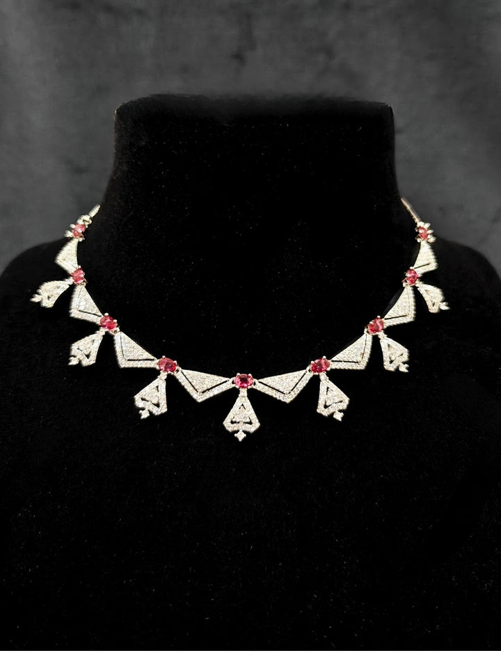 Close-up of an ornate Western Red (Silver Polish) Collar Diamond jewellery set and earrings with American Diamond and Green Colored Stones. Reception-ready look featuring a statement American diamond jewelry set. Party wear outfit completed with a lightweight American diamond necklace.