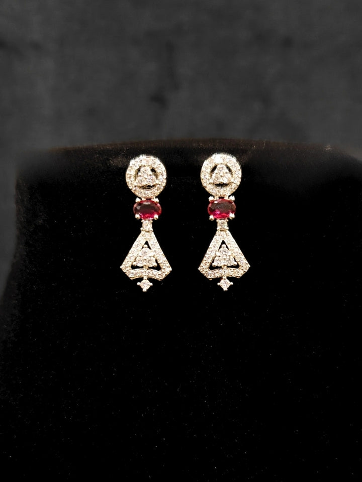 Close-up of an ornate Western Red (Silver Polish) Collar Diamond jewellery set and earrings with American Diamond and Green Colored Stones. Reception-ready look featuring a statement American diamond jewelry set. Party wear outfit completed with a lightweight American diamond necklace.