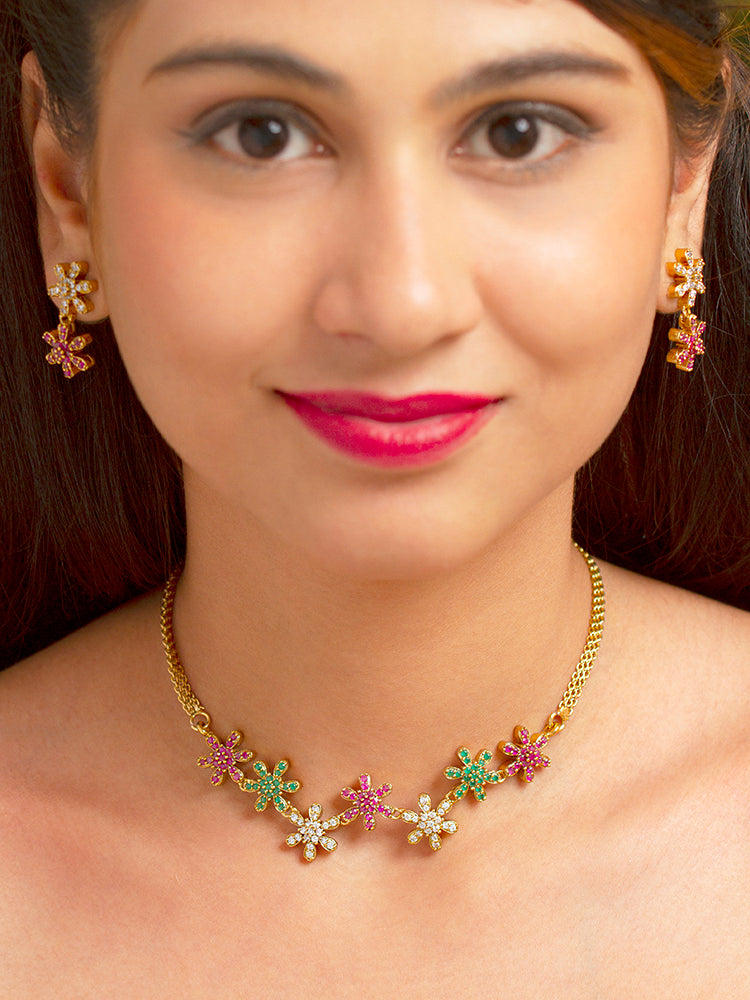 A woman with straight brown hair wears the Aurelia Choker Necklace Set—gold party jewelry with colorful floral designs and American diamonds. She pairs it with matching earrings, bright pink lipstick, and a slight smile.