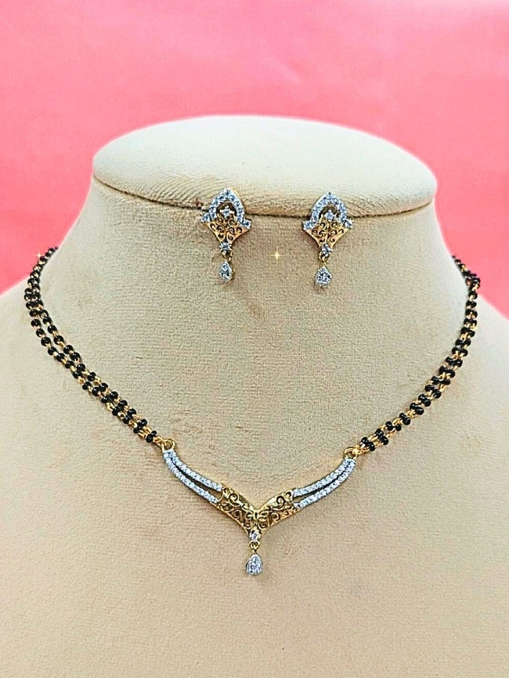 Avantika Mangalsutra—a gold necklace with black mangalsutra beads and matching earrings, pendant featuring sparkling American Diamonds—set against a cream dummy, perfect for your wedding ceremony dress. Diamond mangalsutra. Modern mangalsutra. 