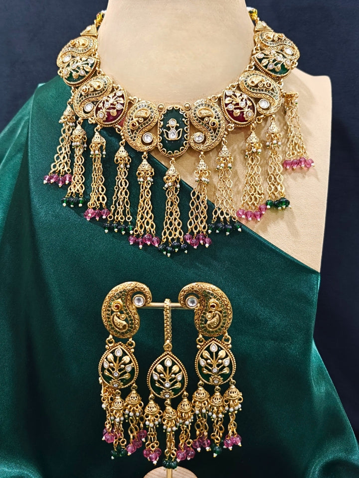 Close-up of an ornate traditional (Gold polish) Green and Mint Pink Collar jewellery set and earrings and maangtikka with Colored Stones, Kundan and Colored Beads. Bride wearing a colorful artificial Colored Stones set for reception night. Wedding function styling with a premium Colored Stone imitation necklace.