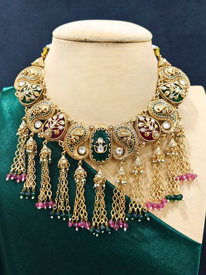 Close-up of an ornate traditional (Gold polish) Green and Mint Pink Collar jewellery set and earrings and maangtikka with Colored Stones, Kundan and Colored Beads. Bride wearing a colorful artificial Colored Stones set for reception night. Wedding function styling with a premium Colored Stone imitation necklace.