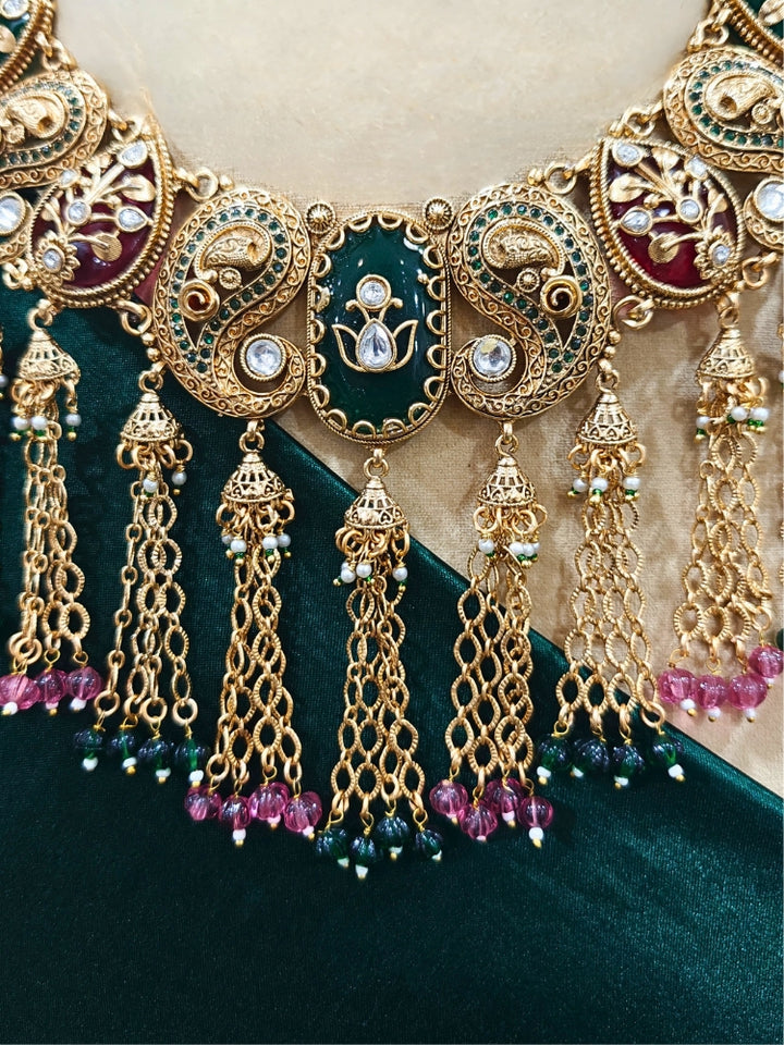 Close-up of an ornate traditional (Gold polish) Green and Mint Pink Collar jewellery set and earrings and maangtikka with Colored Stones, Kundan and Colored Beads. Bride wearing a colorful artificial Colored Stones set for reception night. Wedding function styling with a premium Colored Stone imitation necklace.