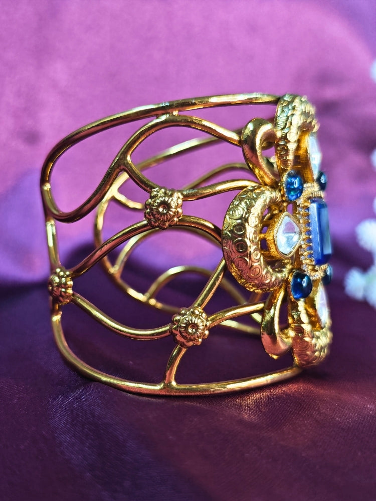 The Aziza Navy Blue Bracelet (Adjustable) showcases an intricate floral design with a large Navy Blue center stone, kundan and smaller Navy Blue colored stones, set against a rich purple background—an ideal choice for wedding jewelry.