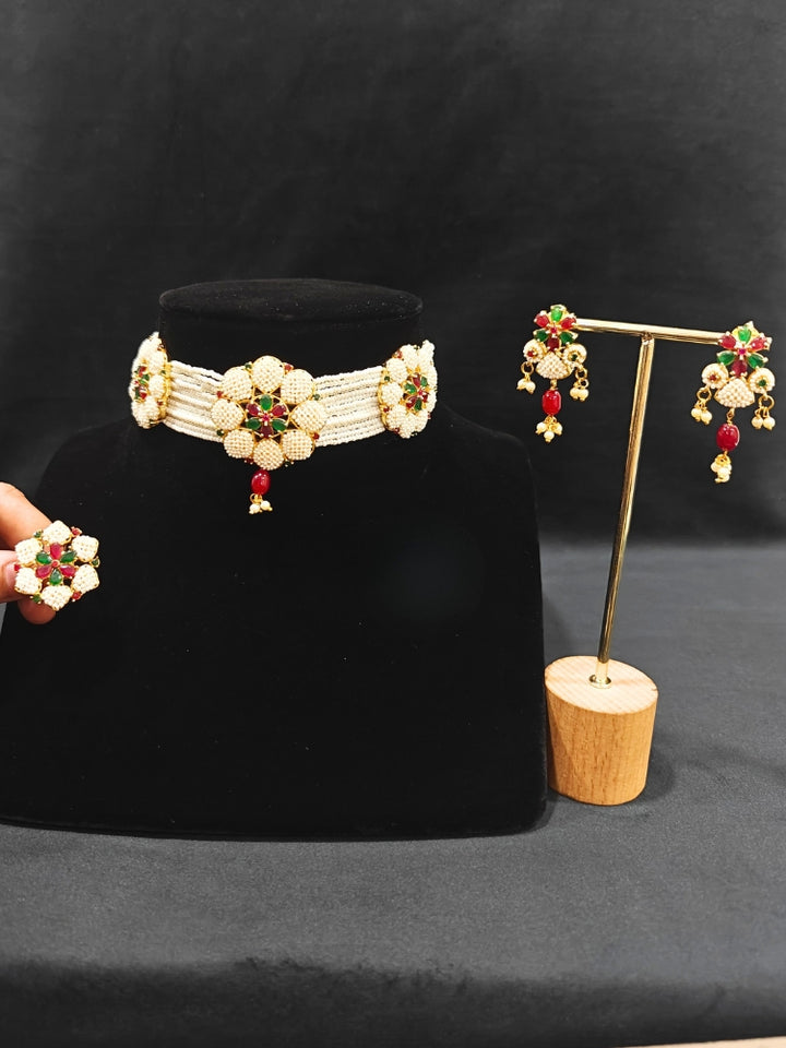 Close-up of an ornate traditional (Bright Gold Polish) Red, Green and White Choker jewellery set and earrings and Ring with Pearls and Red & Green Colored Stones. Mehendi ceremony look completed with a handcrafted Pearl jewelry set. Woman wearing a vibrant Pearl artificial jewelry set for celebrations.