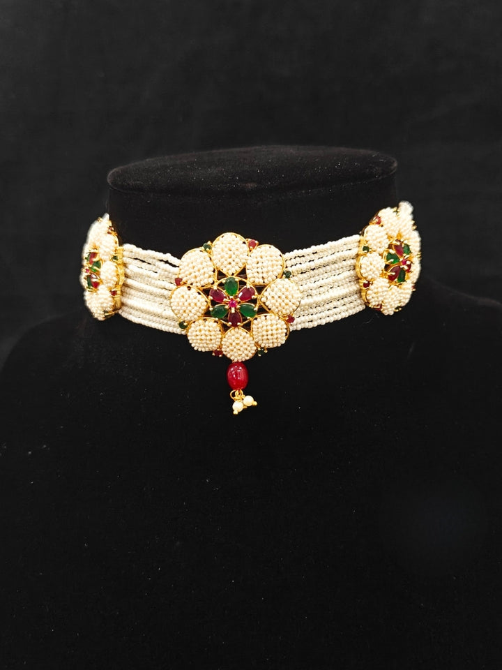 Close-up of an ornate traditional (Bright Gold Polish) Red, Green and White Choker jewellery set and earrings and Ring with Pearls and Red & Green Colored Stones. Mehendi ceremony look completed with a handcrafted Pearl jewelry set. Woman wearing a vibrant Pearl artificial jewelry set for celebrations.