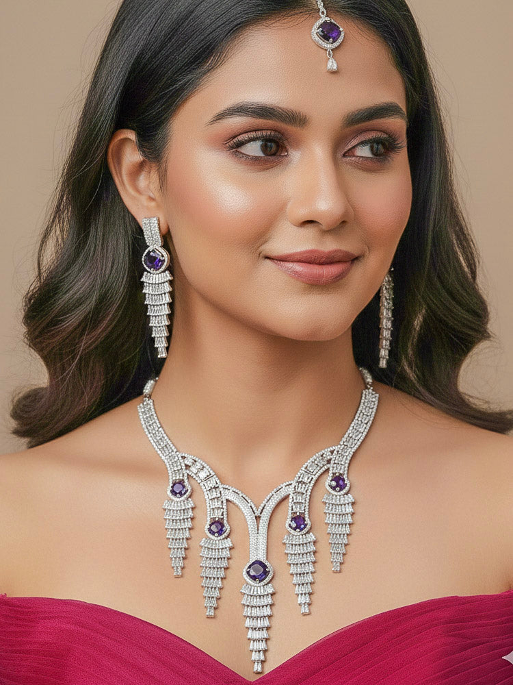"A bride-to-be wearing an exquisite artificial diamond necklace with Purple colored stone and matching earrings and matching maangtikka, designed for the perfect engagement look. This stunning artificial diamond jewelry set offers luxury and sophistication while being an affordable alternative to natural diamonds."
