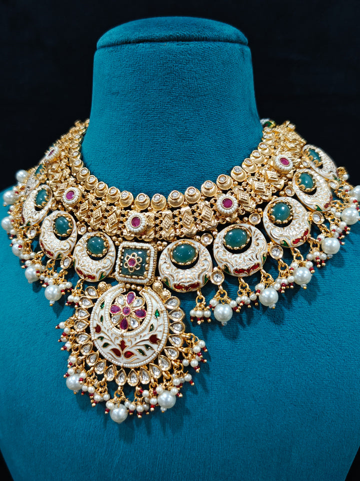 Close-up of an ornate traditional Heritage gold Collar jewellery set and earrings and maangtikka with Pearls, Meenakari, Green Colored Stones and Kundan. Traditional Indian bridal look completed with a heritage artificial jewelry set. Close-up of detailed enamel craftsmanship in Meenakari jewelry.