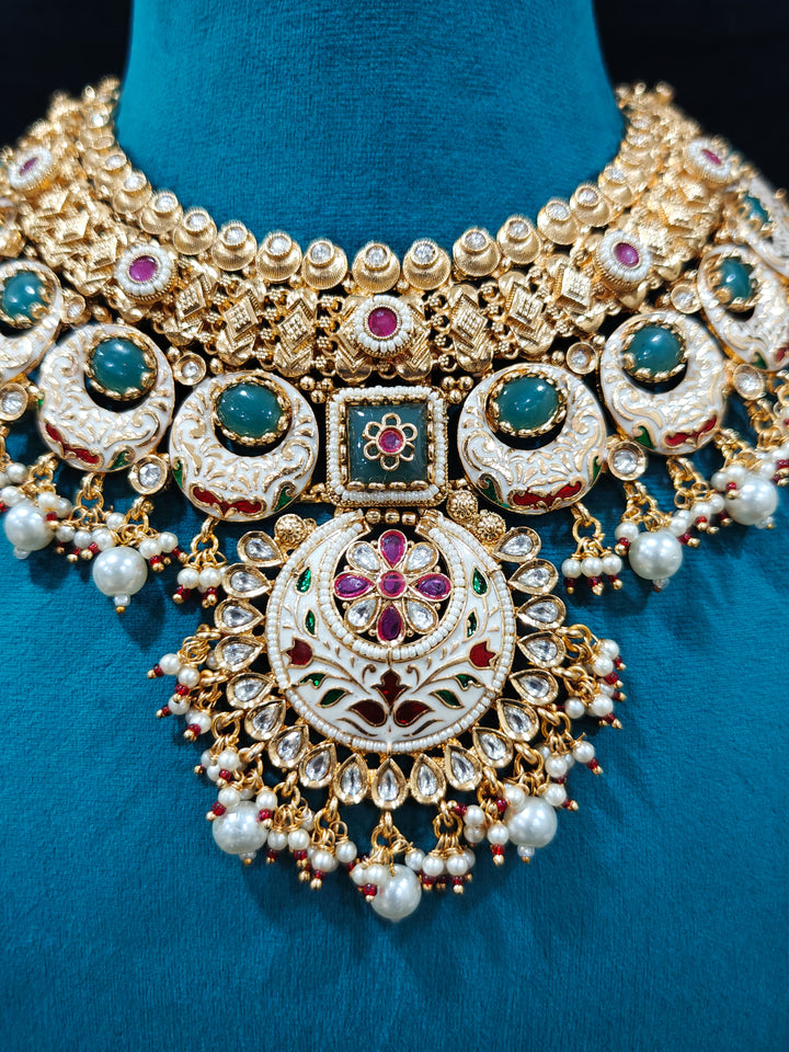 Close-up of an ornate traditional Heritage gold Collar jewellery set and earrings and maangtikka with Pearls, Meenakari, Green Colored Stones and Kundan. Traditional Indian bridal look completed with a heritage artificial jewelry set. Close-up of detailed enamel craftsmanship in Meenakari jewelry.
