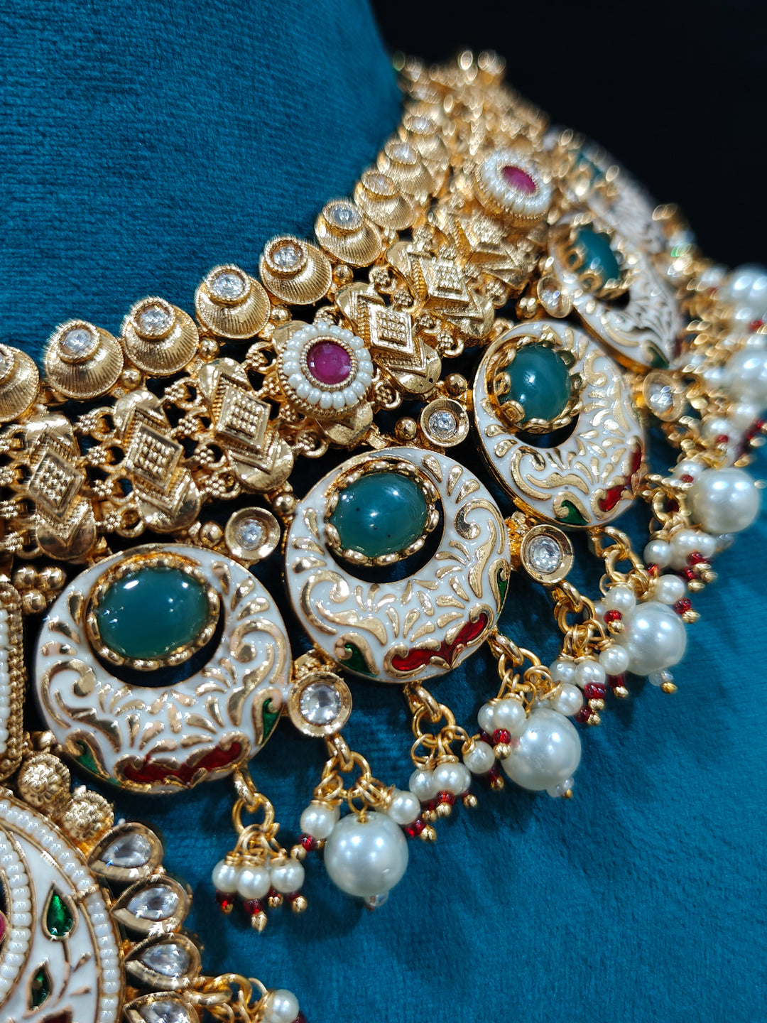 Close-up of an ornate traditional Heritage gold Collar jewellery set and earrings and maangtikka with Pearls, Meenakari, Green Colored Stones and Kundan. Traditional Indian bridal look completed with a heritage artificial jewelry set. Close-up of detailed enamel craftsmanship in Meenakari jewelry.