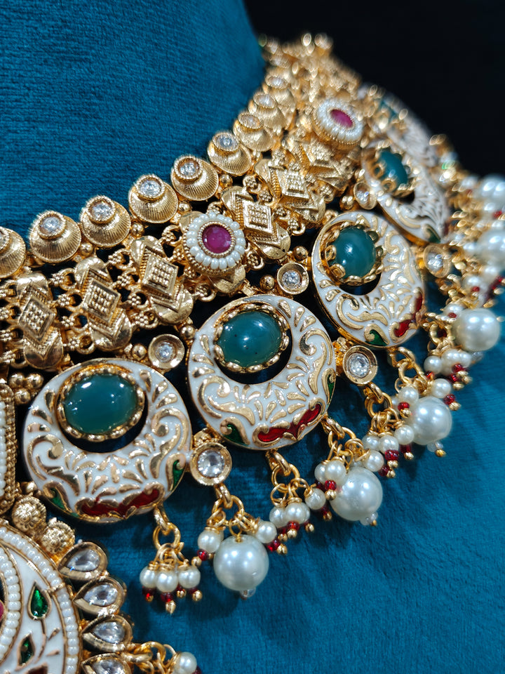 Close-up of an ornate traditional Heritage gold Collar jewellery set and earrings and maangtikka with Pearls, Meenakari, Green Colored Stones and Kundan. Traditional Indian bridal look completed with a heritage artificial jewelry set. Close-up of detailed enamel craftsmanship in Meenakari jewelry.