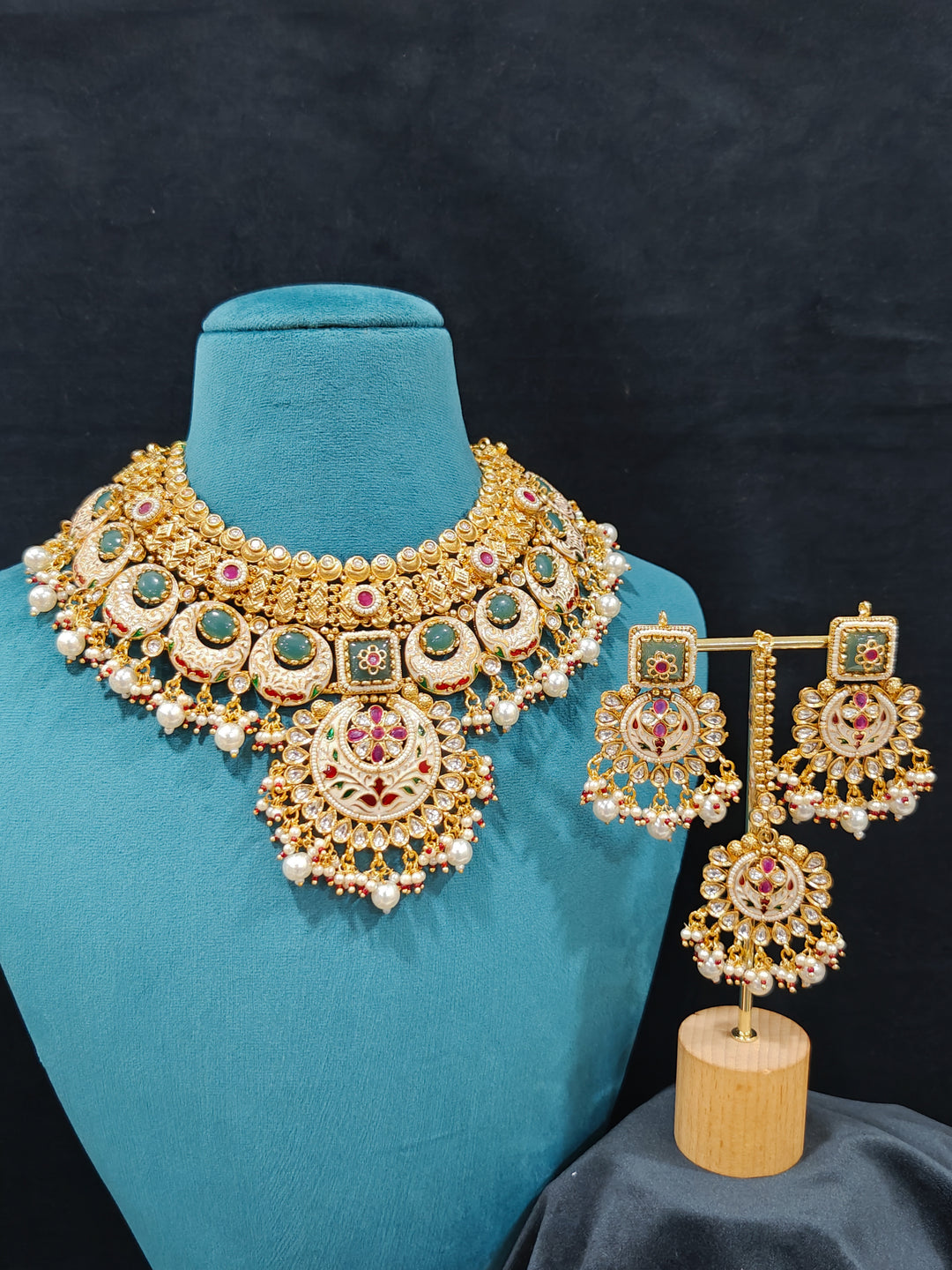 Close-up of an ornate traditional Heritage gold Collar jewellery set and earrings and maangtikka with Pearls, Meenakari, Green Colored Stones and Kundan. Traditional Indian bridal look completed with a heritage artificial jewelry set. Close-up of detailed enamel craftsmanship in Meenakari jewelry.