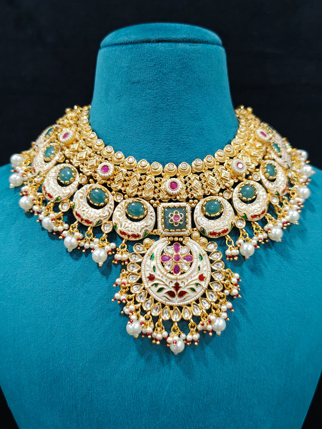 Close-up of an ornate traditional Heritage gold Collar jewellery set and earrings and maangtikka with Pearls, Meenakari, Green Colored Stones and Kundan. Traditional Indian bridal look completed with a heritage artificial jewelry set. Close-up of detailed enamel craftsmanship in Meenakari jewelry.