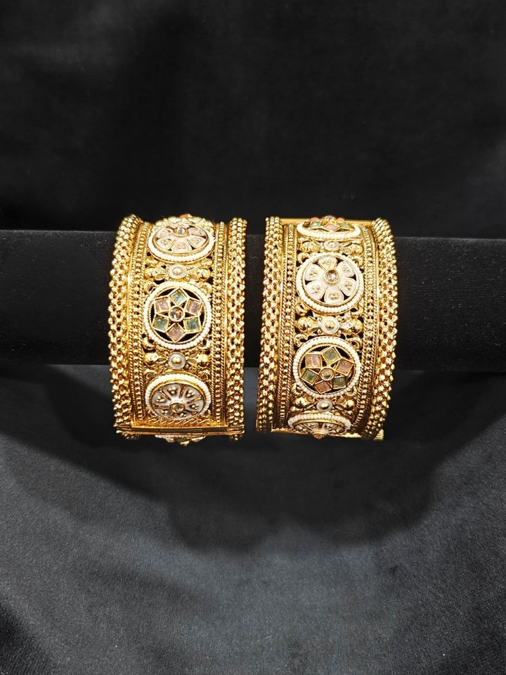 Close-up of an ornate traditional Rajwadi gold Bangle with Mint Pink & Mint Green Colored Stone, Meenakari, Bandhai Work and Pearls. Traditional Indian bridal jewelry look with artificial bangles.
Luxury artificial Rajwadi bangles styled for a wedding function. Close-up of high-quality imitation Meenakari bangles for bridal wear.