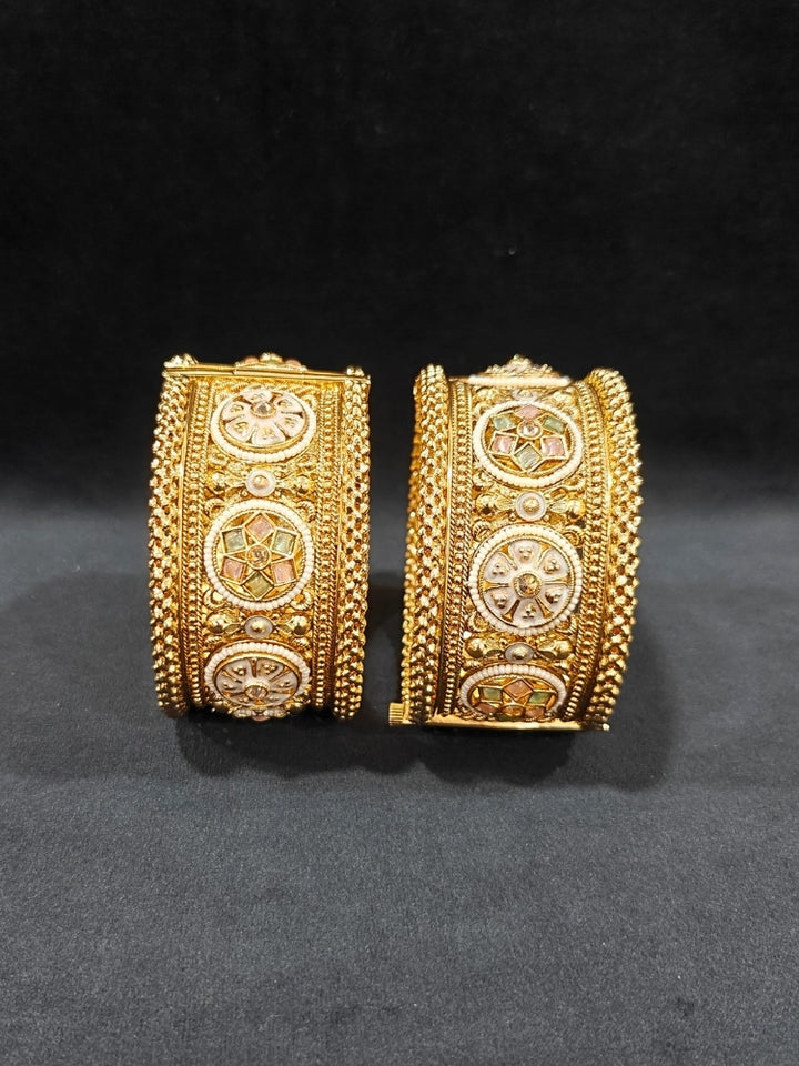 Close-up of an ornate traditional Rajwadi gold Bangle with Mint Pink & Mint Green Colored Stone, Meenakari, Bandhai Work and Pearls. Traditional Indian bridal jewelry look with artificial bangles.
Luxury artificial Rajwadi bangles styled for a wedding function. Close-up of high-quality imitation Meenakari bangles for bridal wear.