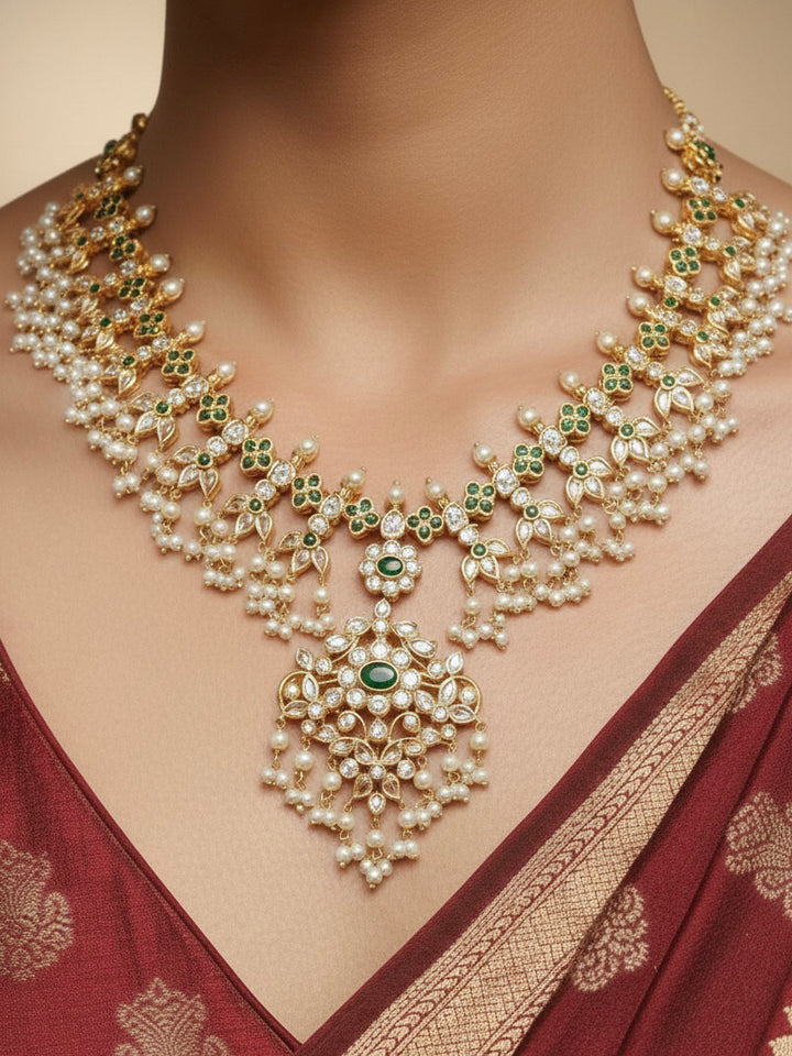 Close-up of a woman wearing an ornate traditional collar jadau gold jewellery set and jadau earrings with pearls , Kundan, Green Color Stone. Saree look enhanced with a traditional Jadau artificial necklace. Bridal styling inspiration with a premium Jadau imitation necklace.