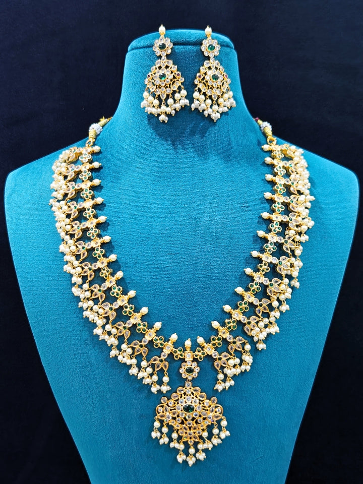 Close-up of an ornate traditional collar jadau gold jewellery set and jadau earrings with pearls , Kundan, Green Color Stone. Mehendi function outfit styled with a Jadau necklace. Close-up of a luxury Jadau imitation necklace styled with a lehenga.
