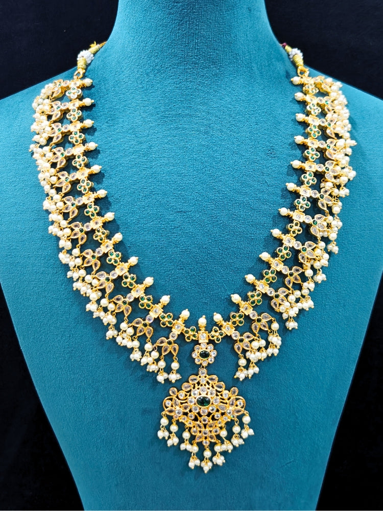 Close-up of an ornate traditional collar jadau gold jewellery set and jadau earrings with pearls , Kundan, Green Color Stone. Mehendi function outfit styled with a Jadau necklace. Close-up of a luxury Jadau imitation necklace styled with a lehenga.