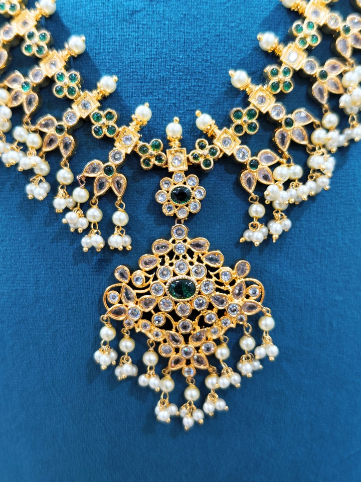 Close-up of an ornate traditional collar jadau gold jewellery set and jadau earrings with pearls , Kundan, Green Color Stone. Mehendi function outfit styled with a Jadau necklace. Close-up of a luxury Jadau imitation necklace styled with a lehenga.