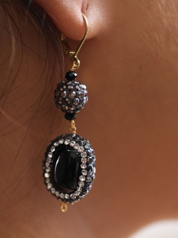 A woman with straight brown hair in Indo-Western attire wears the Black Nebula Long Necklace Set—featuring a patterned black and gold outfit, sparkling earrings, and a layered black beaded necklace—looking neutrally at the camera.