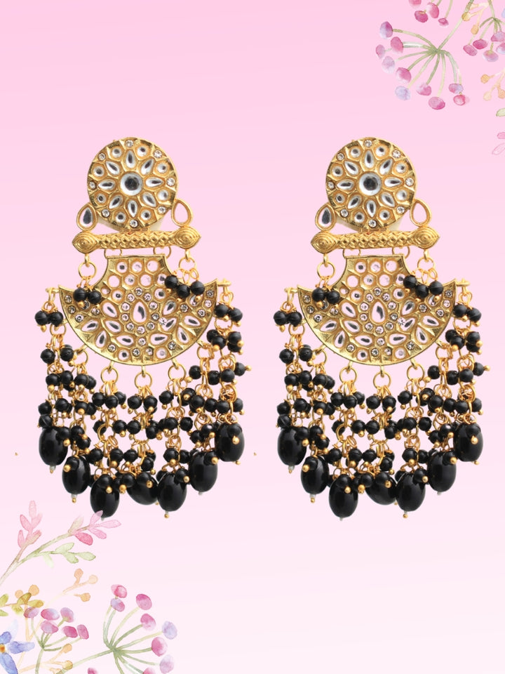 The Black Neha Long Earrings feature ornate Kundan stone detailing in chandbali earrings shape and several dangling black beads, shown against a pastel pink background with floral accents.