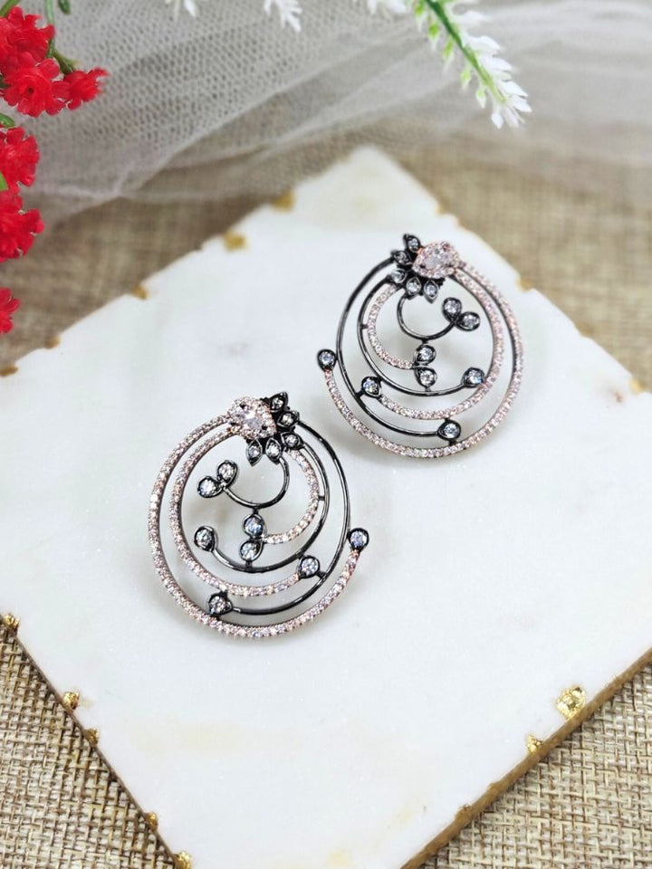 The Black & Pink Maria Earrings feature sparkling circular American Diamonds with intricate spiral designs and clear stones, beautifully displayed on a White surface beside Flowers decor and White Net. American Diamond Earrings