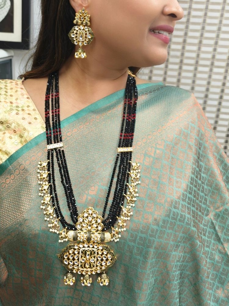 A woman in a traditional Sea Green and gold silk saree wears the Black Shazia Necklace Set with matching earrings and poses in profile with a smile—an elegant choice for a wedding ceremony. Kundan Meenakari pendant hanging with Black crystal stones, and pearls, perfect for weddings. 