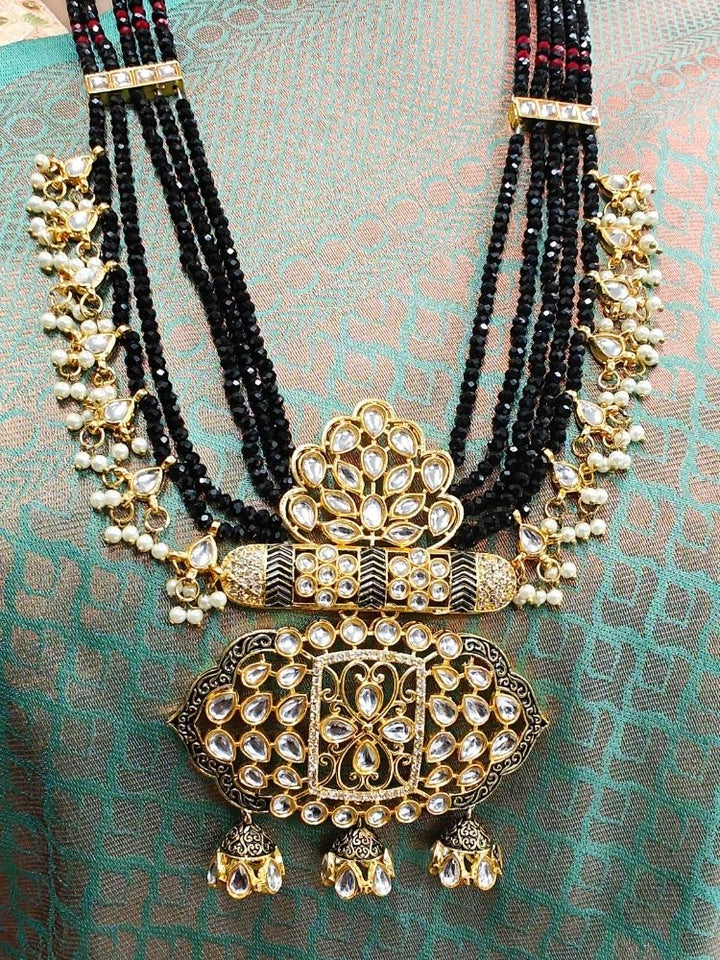 A woman in a traditional Sea Green and gold silk saree wears the Black Shazia Necklace Set with matching earrings and poses in profile with a smile—an elegant choice for a wedding ceremony. Kundan Meenakari pendant hanging with Black crystal stones, and pearls, perfect for weddings. 
