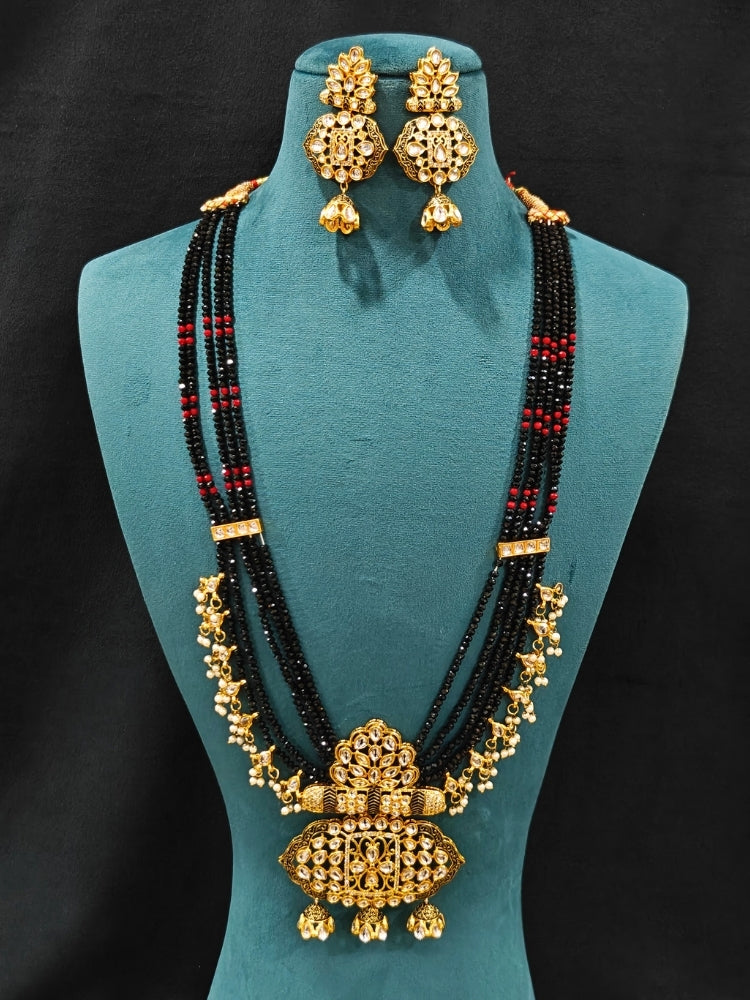 Close-up of an ornate traditional Black Meenakari gold Long jewellery set and earrings with Kundan, Meenakari work, crystal beads, pearls and American Diamonds. Wedding function styling with a premium Meenakari imitation necklace. Close-up of enamel work in Meenakari artificial wedding jewelry.