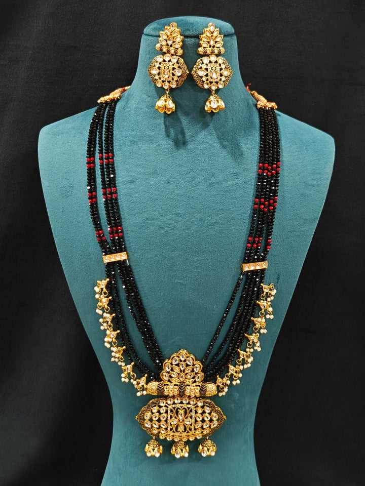 Close-up of an ornate traditional Black Meenakari gold Long jewellery set and earrings with Kundan, Meenakari work, crystal beads, pearls and American Diamonds. Wedding function styling with a premium Meenakari imitation necklace. Close-up of enamel work in Meenakari artificial wedding jewelry.