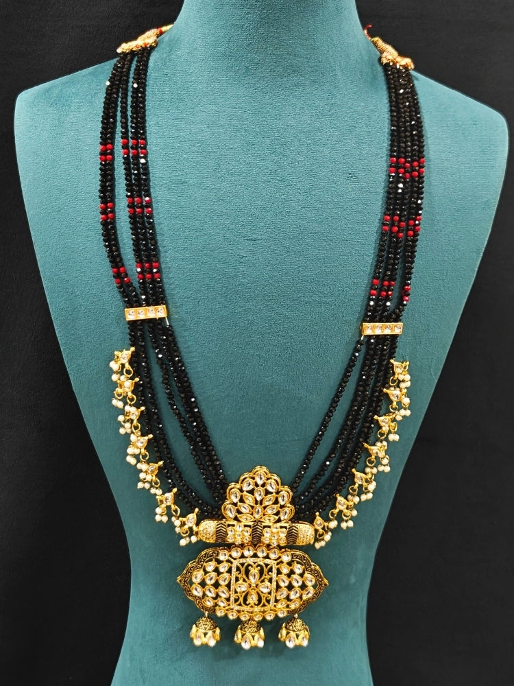 Close-up of an ornate traditional Black Meenakari gold Long jewellery set and earrings with Kundan, Meenakari work, crystal beads, pearls and American Diamonds. Wedding function styling with a premium Meenakari imitation necklace. Close-up of enamel work in Meenakari artificial wedding jewelry.