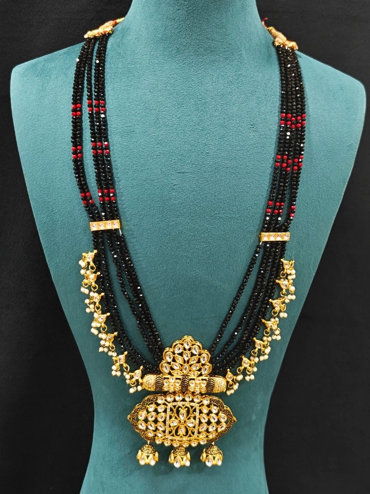 Close-up of an ornate traditional Black Meenakari gold Long jewellery set and earrings with Kundan, Meenakari work, crystal beads, pearls and American Diamonds. Wedding function styling with a premium Meenakari imitation necklace. Close-up of enamel work in Meenakari artificial wedding jewelry.
