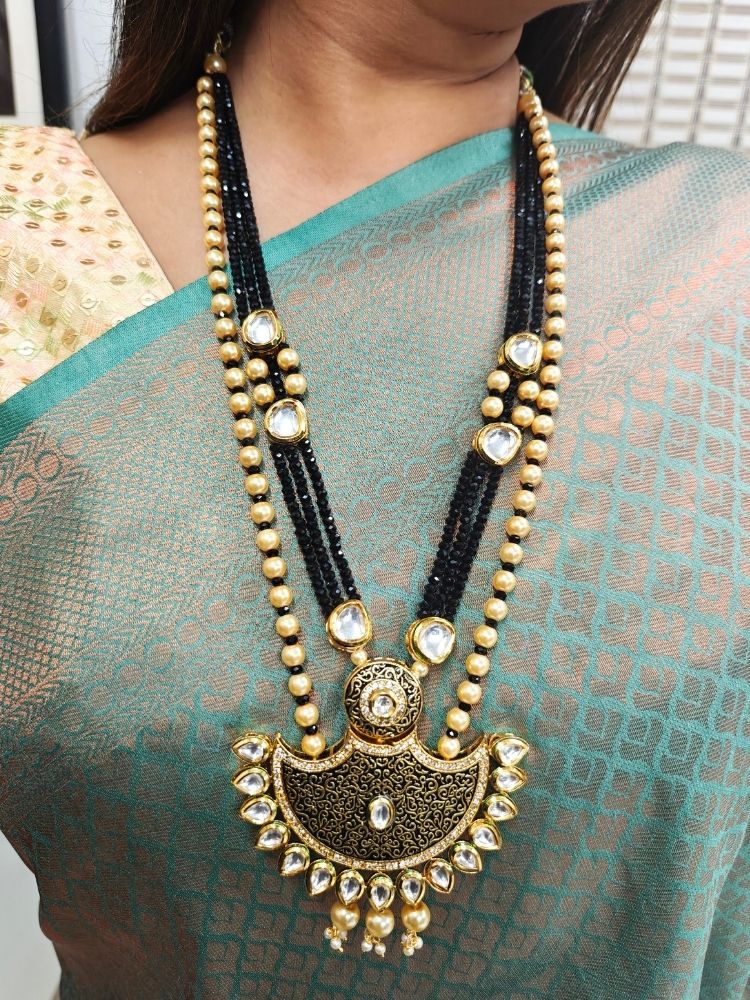 Close-up of a woman wearing an ornate traditional Black Meenakari Long  jewellery set and earrings with Kundan, Meenakari work, crystal beads, pearls and American Diamond. Mehendi ceremony look completed with a Meenakari jewelry set. Woman wearing a vibrant Meenakari artificial jewelry set for celebrations.