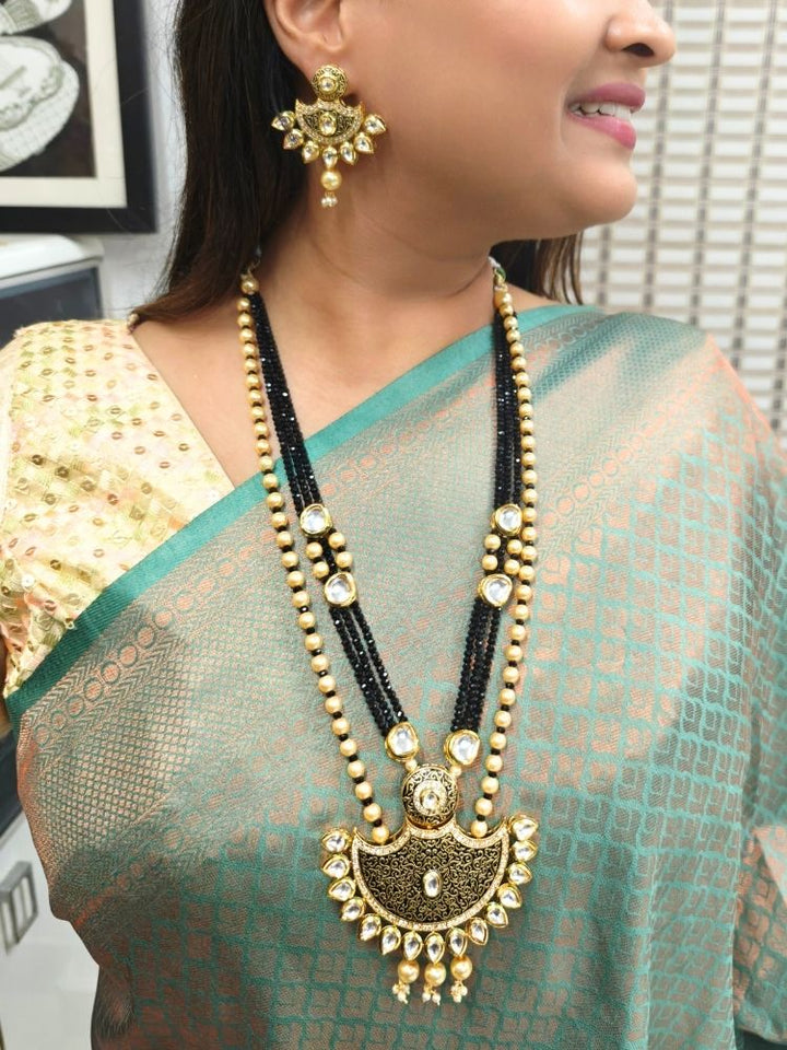 A girl in a deep sea gree  sari showcases the Black Zareen Necklace Set, featuring gold and black tones with pearl accents, matching earrings, intricate designs, american diamonds, and elegant Kundan detailing.