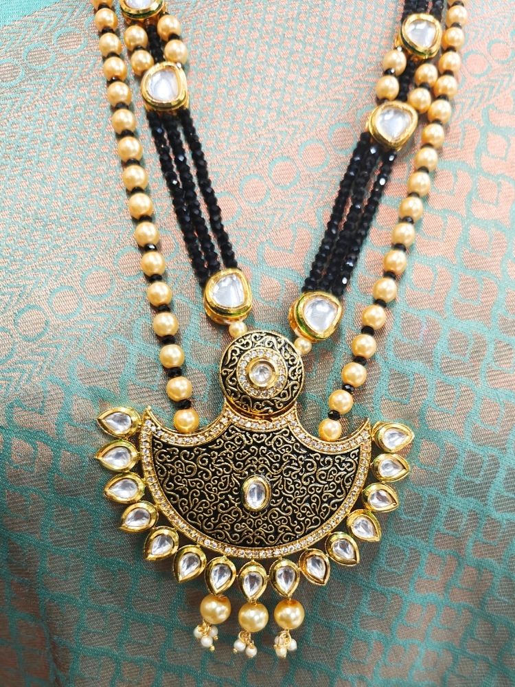 A girl in a deep sea gree  sari showcases the Black Zareen Necklace Set, featuring gold and black tones with pearl accents, matching earrings, intricate designs, american diamonds, and elegant Kundan detailing.