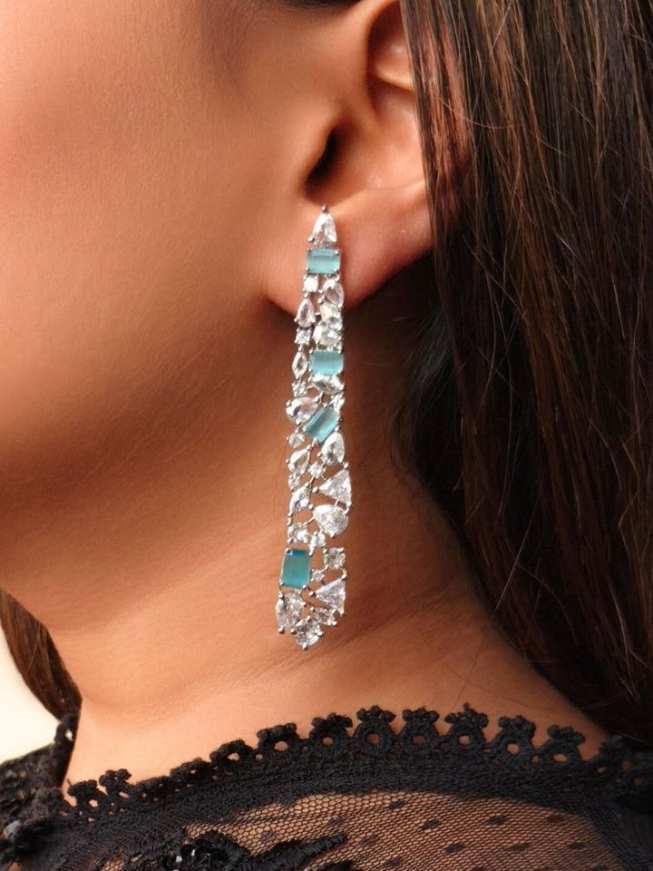 A close-up of a woman with dark hair in a black lace top, wearing Blue Samara Earrings—long, elegant American Diamond  and Blue colored stone long earrings—perfect to pair with a party dress.