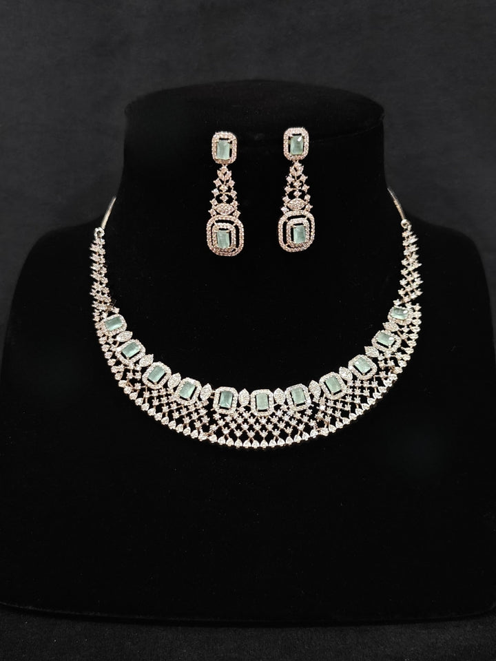 Close-up of an ornate Western Mint Green (Silver Polish) Collar Diamond jewellery set and earrings with American Diamond and Mint Green Colored Stones. A lightweight American diamond necklace perfect for long wedding functions. 