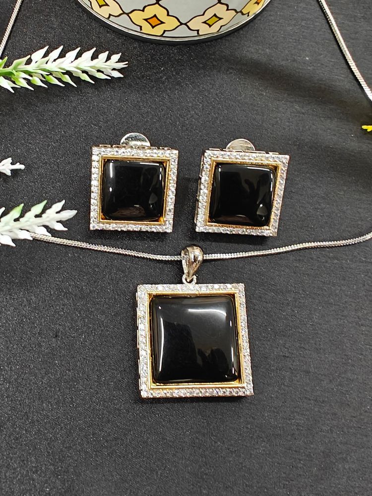 The Carter Black Pendant Set features a square black pendant and matching earrings with silver frames surrounded by American diamonds, displayed on black near a candle and flowers—an elegant ethnic jewelry piece for any occasion. Perfect for casual weal. Casual pendant set. 