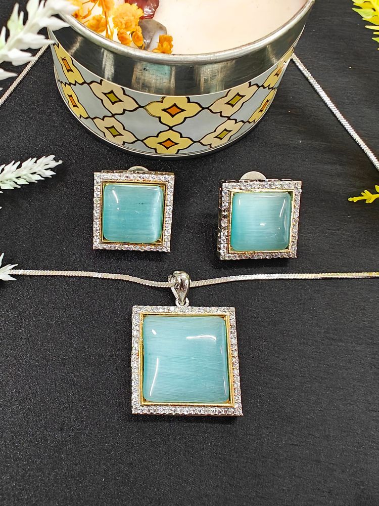 The Carter Blue Pendant Set features a square blue pendant and matching earrings with silver frames surrounded by American diamonds, displayed on black near a candle and flowers—an elegant ethnic jewelry piece for any occasion. Perfect for casual weal. Casual pendant set. 
