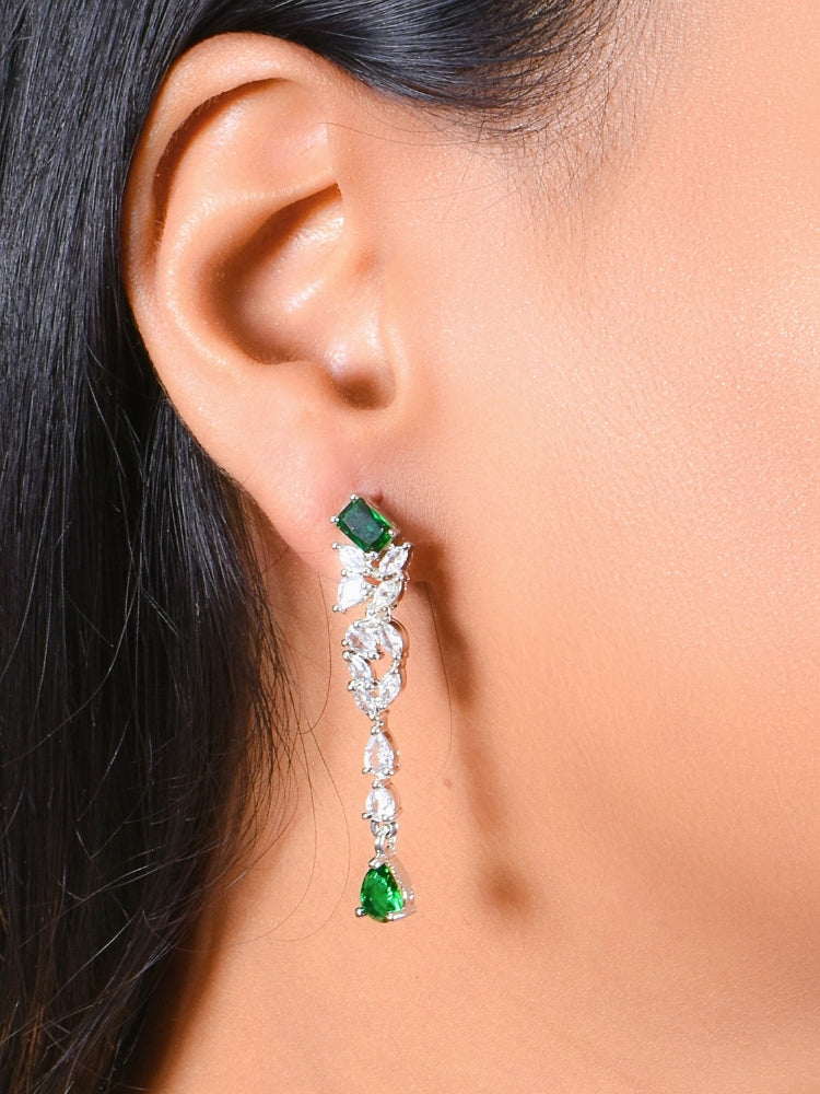 A woman wears the Celestia Green Necklace Set—an American Diamond necklace and matching green gemstone earrings—with a black top. The elegant set is perfect for weddings, complemented by her glossy pink lipstick.